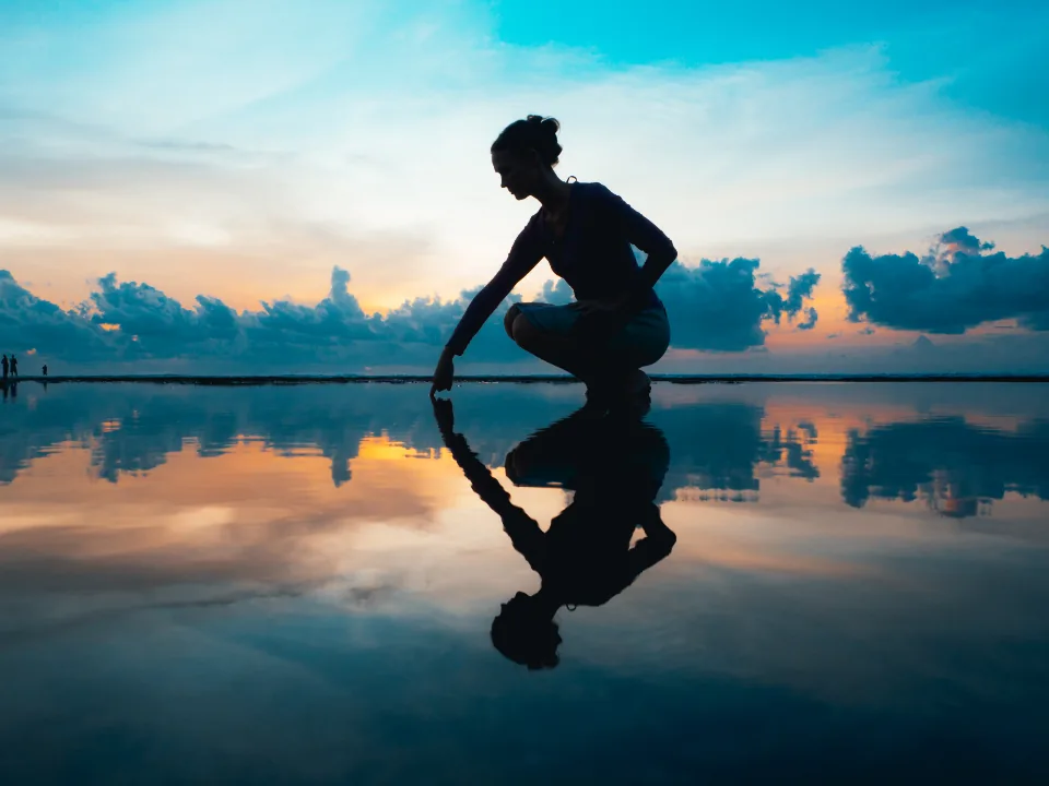 A person's silhouette mirrored in still water at sunset