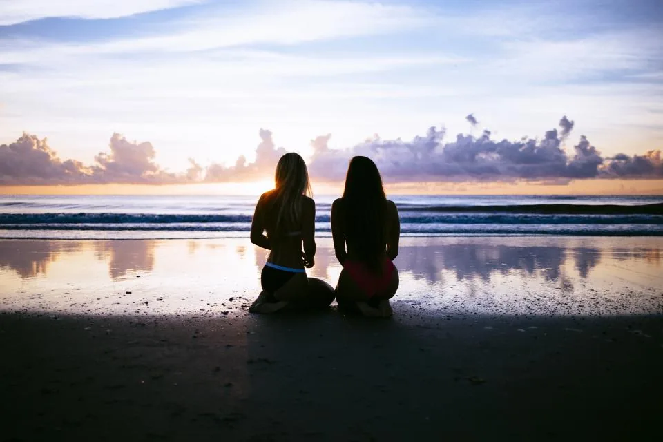 Two friends sitting together watching the sunrise over the shore